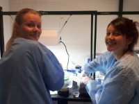 Emily & Molly in the lab, looking back to the camera, wearing blue coats