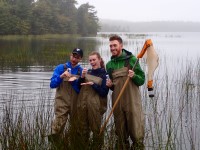 Emma in middle with two other students posing in waders in a lake.