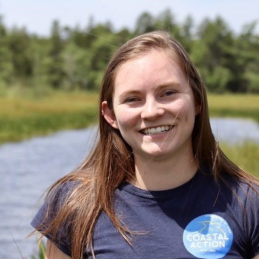 Kaylee wearing a Coastal Action t-shirt with a conifer-edged water landscape behind her