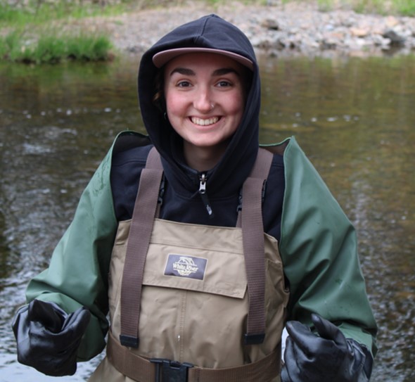 A young woman wearing raincoat and waders standing in a stream.