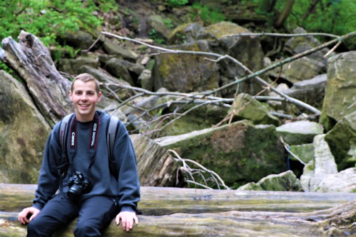 A person wearing a blue top and a camera sitting on a fallen log
