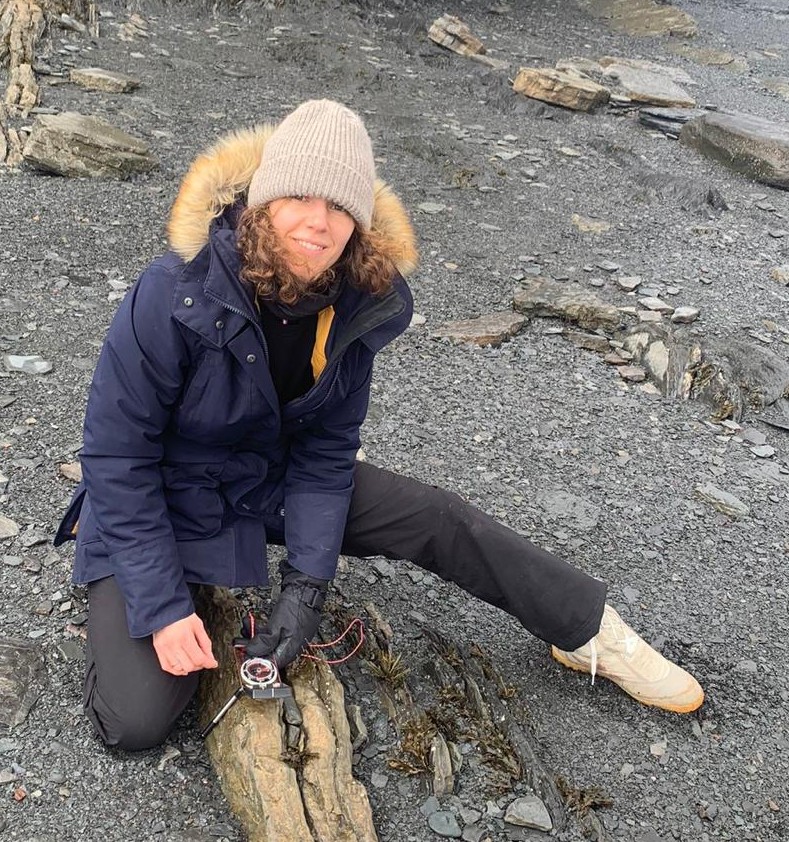 Anna wearing warm clothing on a cobblestone beach taking measurements