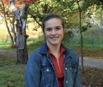 Lucinda standing in front of a small wooded grove with some autumn leaf colours in back.