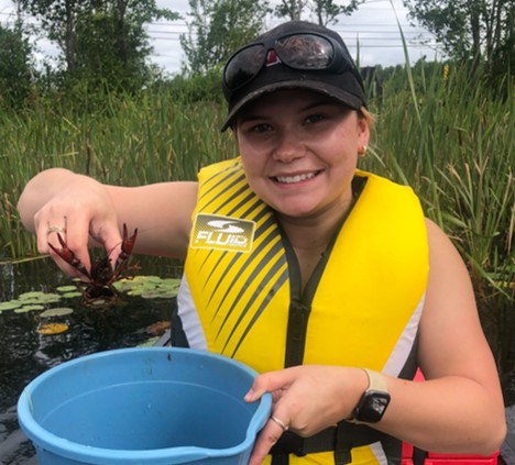 Madison wearing a lifejacket in a canoe, holding up a crayfish