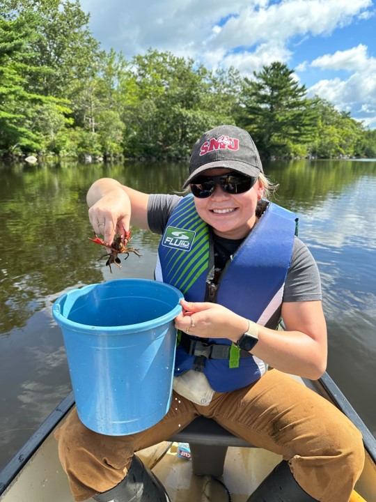 A woman in a canoe, holding up a crayfish above a bucket