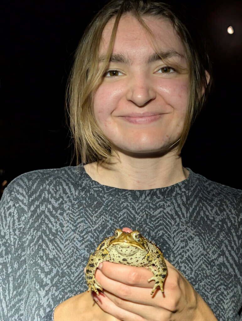 Mallory Jarvis in the field holding up a frog with a smile