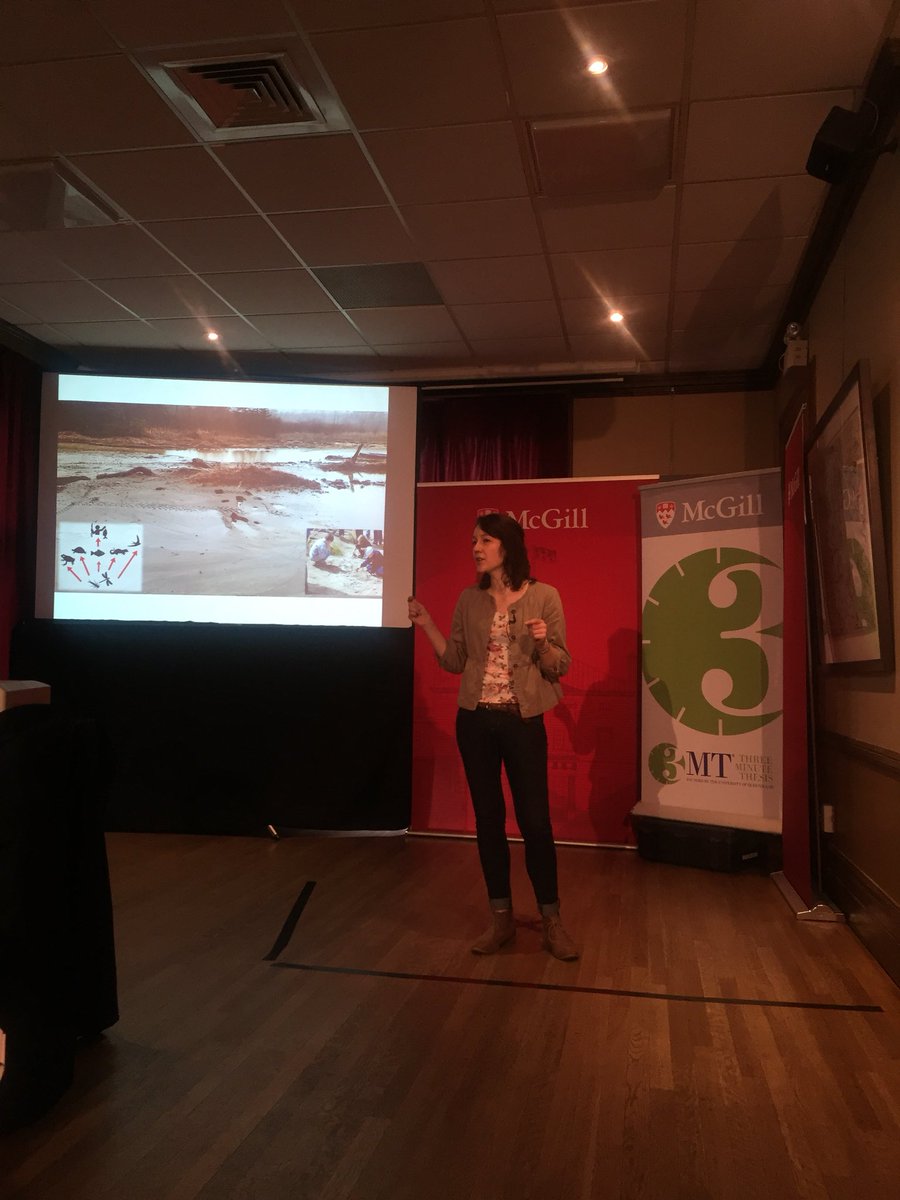 Molly LeBlanc presenting her three minute thesis talk, with a slide of an abandoned gold mine impacted wetland above her.