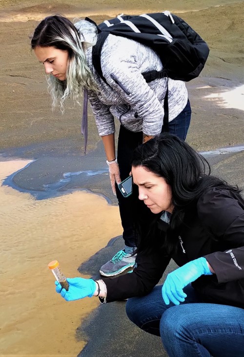 WhiteFeather sampling a puddle in a contaminated legacy gold mine site while Brittany looks on.